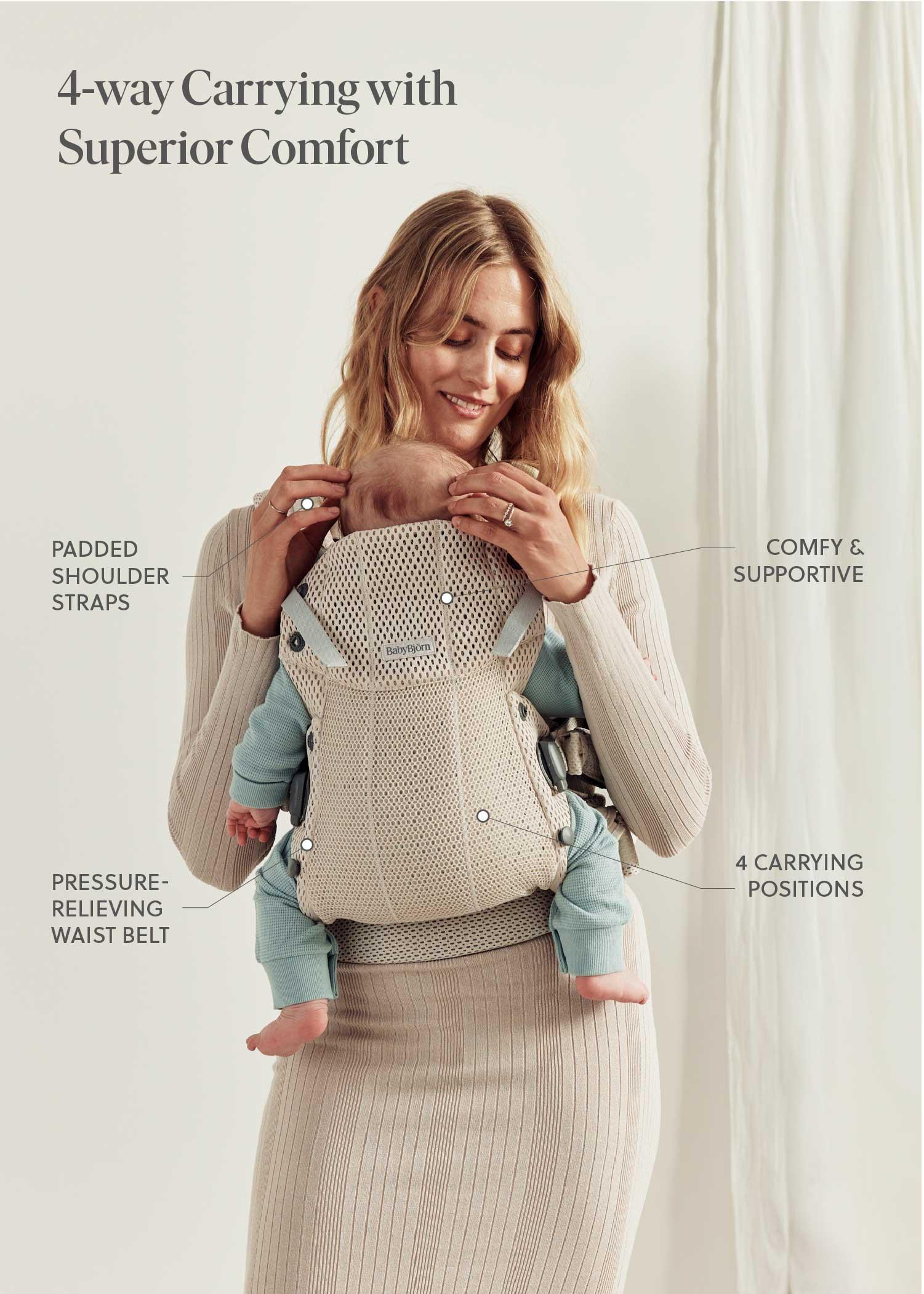 A woman wearing a beige baby carrier with a baby, featuring padded shoulder straps, a waist belt, and offers four carrying positions.